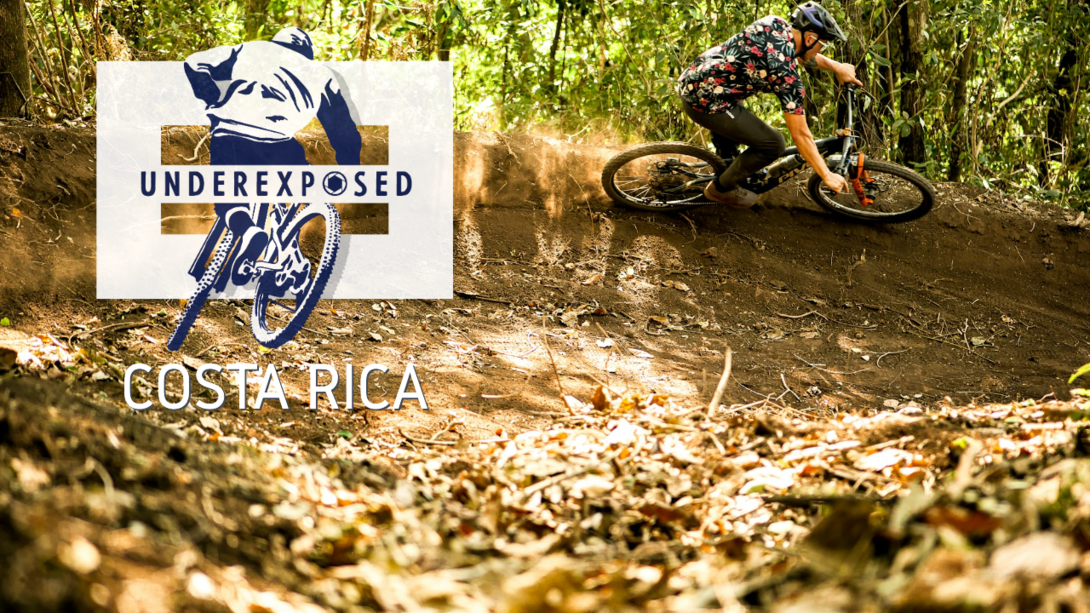 Mountain biker in a right handed berm, with a trail of dust behind him and the Underexposed logo with Costa Rica beneath of it.